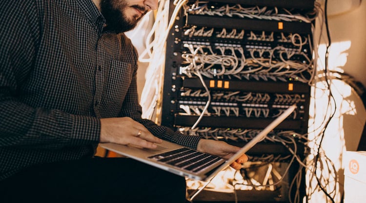 Man uses laptop, server kabinet is open and cables are visible