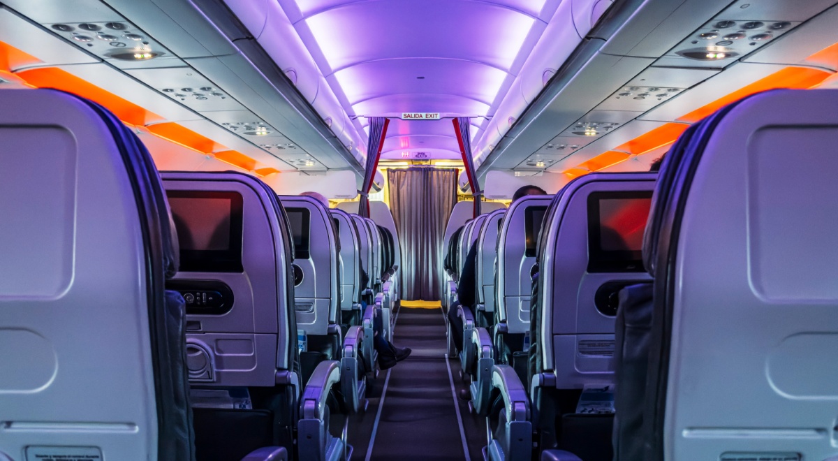 12 grey plane seats inside of plane, orange light, grey curtains, blue lines