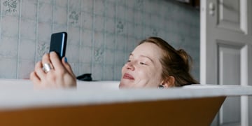ginger smiling woman in bath, scrolling through phone, blue tiles