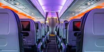 12 grey plane seats inside of plane, orange light, grey curtains, blue lines